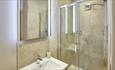 En suite with stone coloured tiles. Mirror with lights on the wall. White sink and walk in shower.