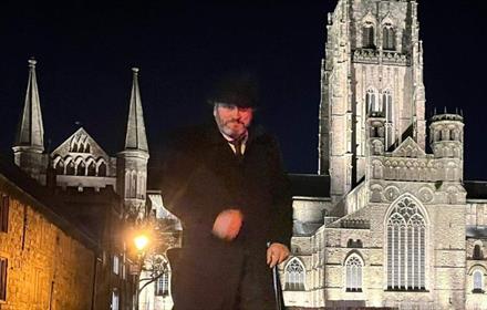 Andrew Ross (Tour guide) standing n front of Durham Cathedral on a dark evening