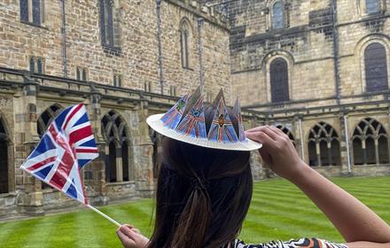 Girl waving a flag, wearing a homemade paper crown, standing in Cathedral Cloisters.