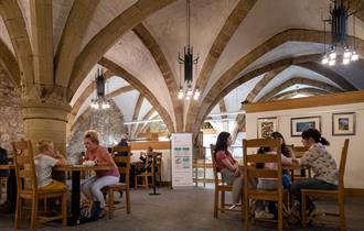 Two families sit at tables in a cafe, which has an arched stone roof.
