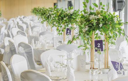 White tables and chairs with green table displays, cutlery, serviettes