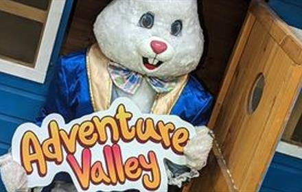 Someone dressed as an Easter bunny holding an Adventure Valley sign