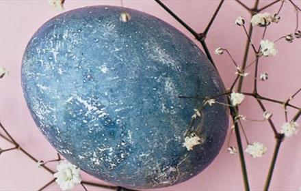 Blue egg surrounded by branches of blossom. Light pink background