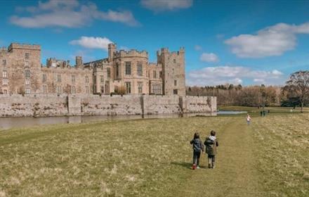 Raby Castle and lake. Children walking in the Deer Park. Blue sky with cloud.