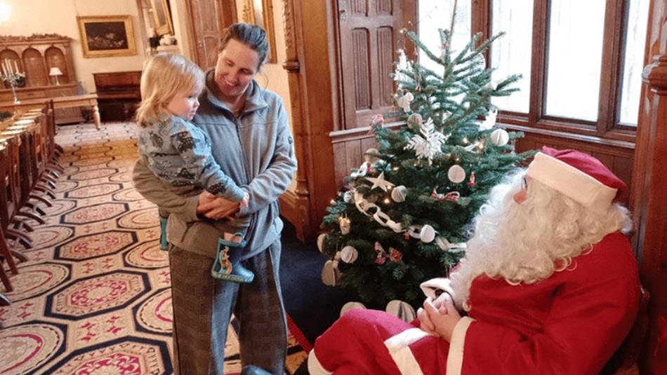 Father Christmas sitting beside a Christmas Tree, talking to a child being held by a woman. Father Christmas sitting beside a Christmas Tree, talking to a child being held by a woman.