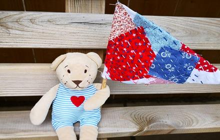 A teddy bear holding a patchwork fabric flag