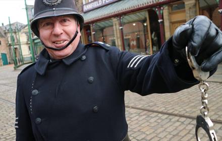 Image of a staff member at Beamish dressed as a police officer holding handcuffs.