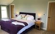 Bedroom with double bed, bedside tables either side with purple lamps on