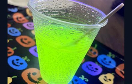 Plastic cup with green fizzy drink on a table cloth with coloured pumpkins