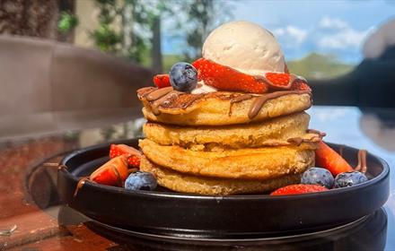 Image of a delicious stack of pancakes topped with blueberries and icecream.