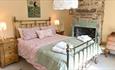 A double bedroom with an open fireplace and a metal bedframe. Pink, floral bedding with a sage green throw over the bottom of the bed. 

