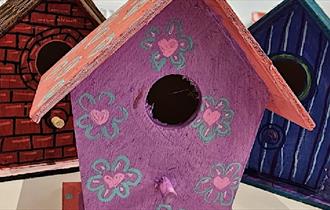 Painted birdhouses with different designs in purple, blue and brown.