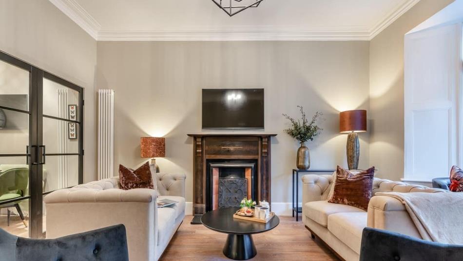 Light coloured living area with a fireplace as a focal point. 2 Large beige sofas place either side of a black coffee table and 2 navy armchairs