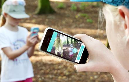 Girl using her phone to find an augmented reality dinosaur in Hardwick Park. Another girl looking at her phone.