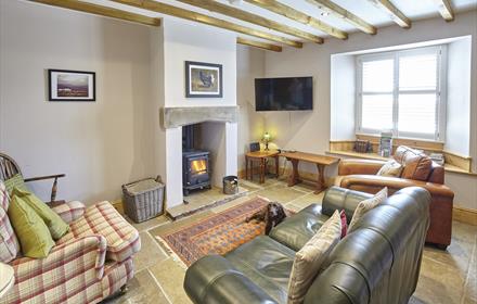 Cosy living are in cottage with real log burner, stone tiled floor and green leather sofa. Wooden beams on the ceiling.