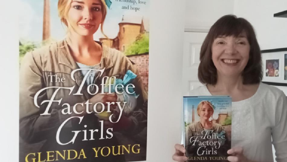 Author Glenda Young, smiling and holding a copy of her new novel, 'The Toffee Factory Girls'.