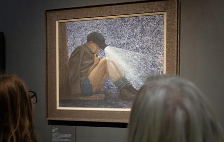 Image of two visitors looking at a painting of a very young miner wearing a miner's helmet and torch.