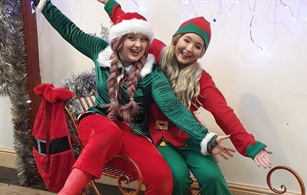 Two women dressed as Elves sitting on a sleigh