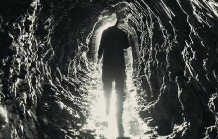 Black and white artwork of man walking through a coal mine