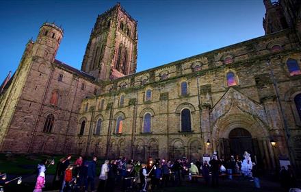 Durham Cathedral with people taking part in lantern parade walking towards entrance