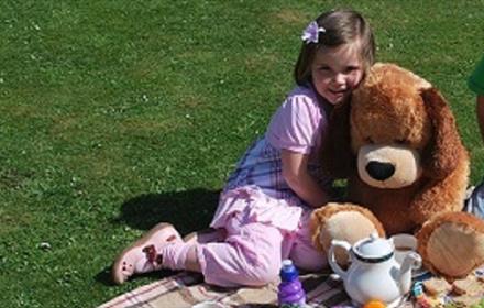 Image of a girl hugging a large teddy bear whilst enjoying a picnic.