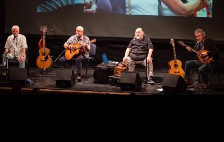 'The Pitmen Poets' performing on stage. Image of the musicians with their guitars.