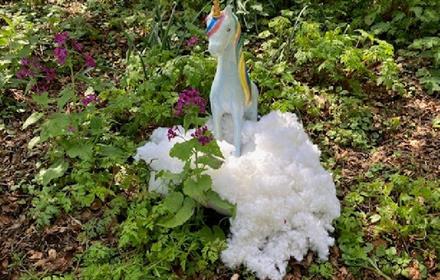White toy unicorn on vegetation on the ground.
