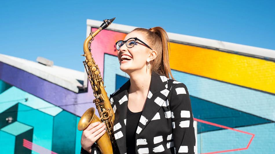 A woman holding a saxophone, in front of a geometric background.