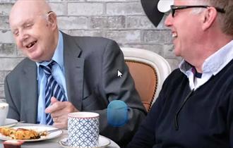 Two gentleman enjoying each other's company over tea and refreshments.