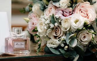 Image of a pink and white wedding bouquet next to some Dior perfume at South Causey Inn.