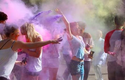 Multi-coloured powder throw at Holi Festival, people laughing and smiling.