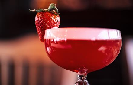 A fruity, red cocktail decorated with a strawberry.