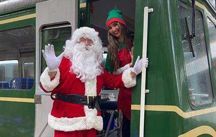 A man dressed as Santa and women dressed as an Elf standing at doorway of a train