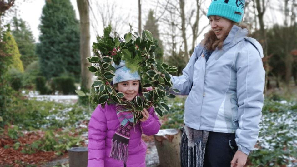 A young girl holding a Christmas Wreath, standing beside a woman outdoors. A young girl holding a Christmas Wreath, standing beside a woman outdoors.