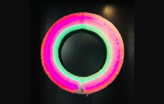 Image of a neon pink ring containing inner green and orange rings also against a black background.