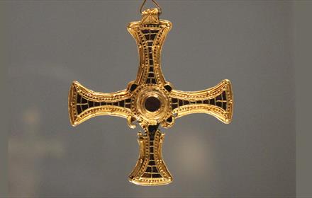 A gold cross pendant with arms inlaid with precious stones.