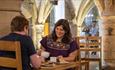 man and woman eating cake and drinking hot drink inside Durham Cathedral undercroft restaurant.