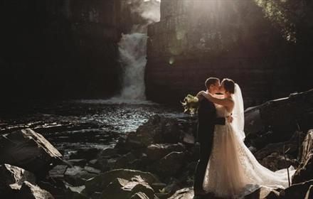 Married couple sharing a kiss on their special day at High Force Waterfall.