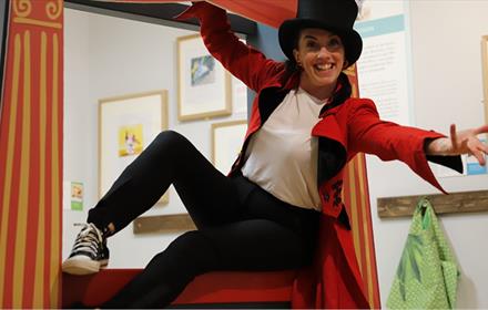 Woman dressed in top-hat, red coat and black trousers.