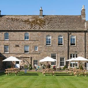View of the Lord Crewe Arms on a bright sunny day with people sat in the garden under white umbrellas.