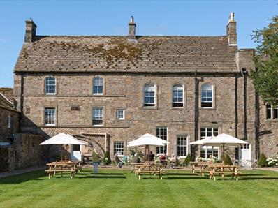 View of the Lord Crewe Arms on a bright sunny day with people sat in the garden under white umbrellas.