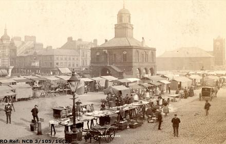Photograph of South Shields Market Place, c.1900 
Image of several people in traditional clothing and market stalls.