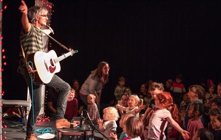 Photo of Nick Cope on stage with guitar entertaining families at concert.