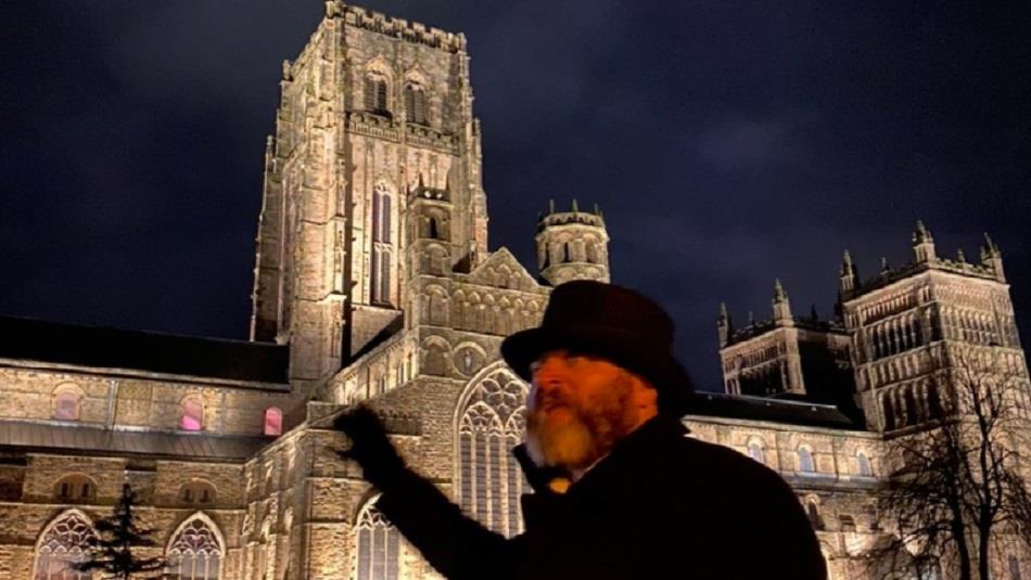 Image of tour guide standing outside of Durham Cathedral at night.