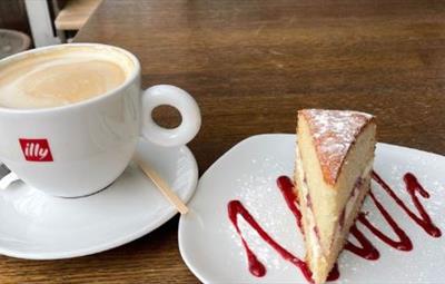 A cup of coffee next to slice of cake on a plate.