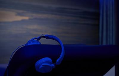 Headphones hooked onto the back of a lounger in darkened room with atmospheric image of coast