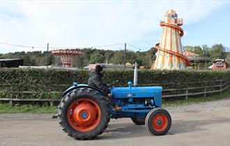A blue tractor in front of the Fairground at Beamish Museum.