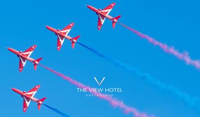 Four red arrows jets flying alongside each other on a clear blue sky with red and blue vapour trails following the jets