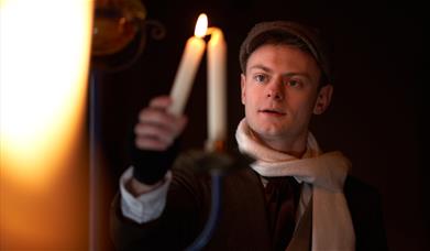 A character from A Christmas Carol holds a candle