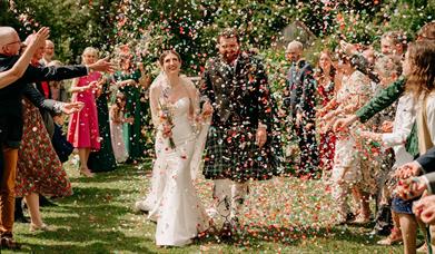 Bride and groom walk down the aisle while guests throw confetti at them